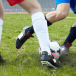 Image of footballers legs kicking soccer ball on stadium