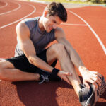 Young male runner suffering from leg cramp on the track at the stadium